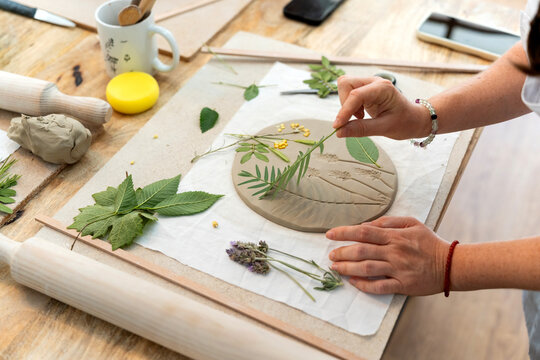 Crafting unique ceramic pieces, hands decorating clay with plants and leaves