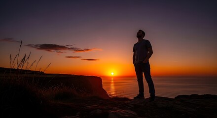 Obraz premium Man silhouetted against a vibrant sunset sky by the ocean horizon