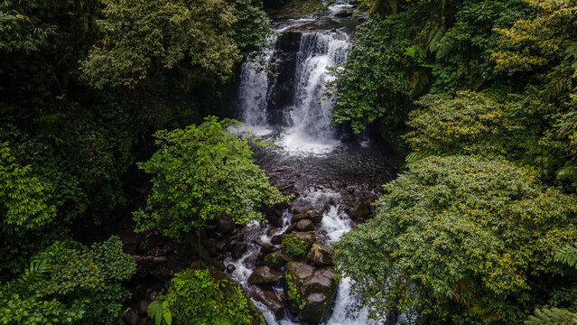 Aerial view of Ambyar waterfall cascading through a lush tropical forest with dense green foliage and rocky stream bed in Purwokerto, Central Java, Indonesia.