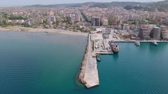 Aerial video of the coastal city of Vlora, Albania, showcasing the deep blue Ionian Sea, city harbour with piers, and beachfront development.