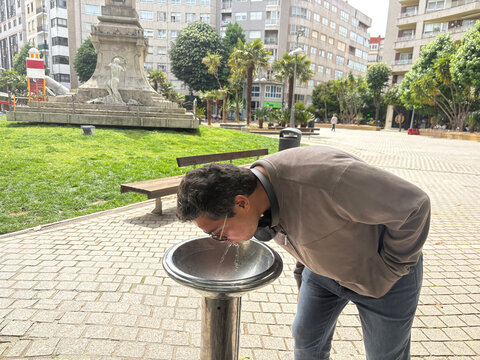 Young man drinking water from public fountain in urban park