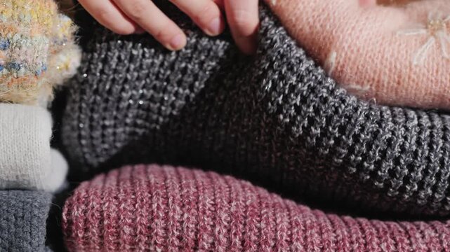 Woman hands touching and sorting stack of warm knitted winter sweaters on wooden background.
