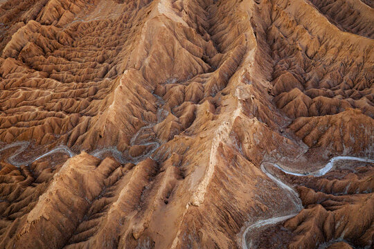 Aerial view of the eroded red rock formations and sharp mountain ridges of Mars Valley with a winding road in San Pedro de Atacama, Antofagasta, Chile.