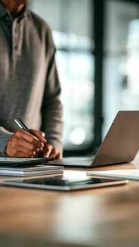 Confident businessman organizing paperwork and using technology for productivity in a bright office setting. Modern workspace setup with digital devices and essential business documents on the desk