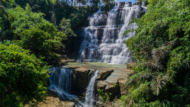 Aerial view of Cigangsa Waterfall cascading over tiered rock formations surrounded by lush tropical forest and green trees Sukabumi, West Java, Indonesia.