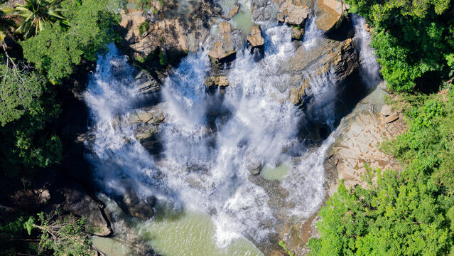 Aerial view of Cigangsa Waterfall cascading over dark rock formations surrounded by lush tropical forest in Sukabumi, West Java, Indonesia.