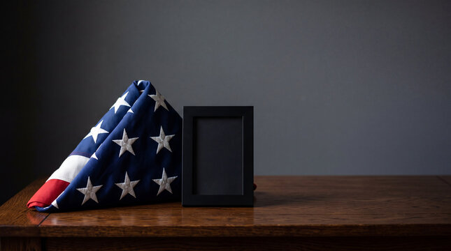 Folded United States flag with empty picture frame on wooden table. Patriotic memorial symbol for deceased soldier. Concept of national remembrance, tribute, respect and honor holiday.