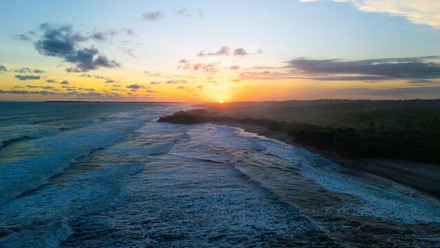 Aerial view of Ujung Genteng Beach with crashing waves, lush coastal vegetation, and a vibrant sunset over the horizon Sukabumi, West Java, Indonesia.