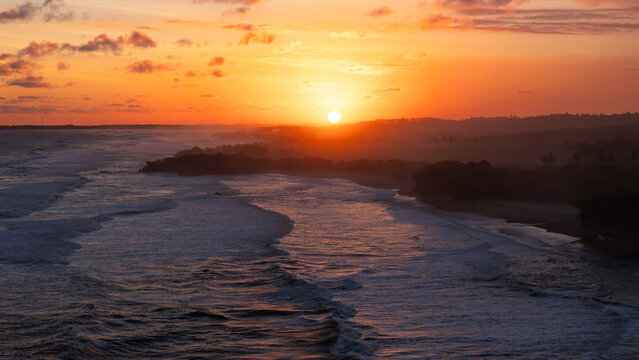 Aerial view of Ujung Genteng Beach with waves crashing on the shore under a vibrant golden sunset sky Sukabumi, West Java, Indonesia.