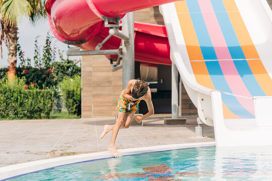 Child jumping and dives in swimming pool at sunny day. Kid boy refreshing and playing at heat weather, active vacation and healthy lifestyle. Happy summer.