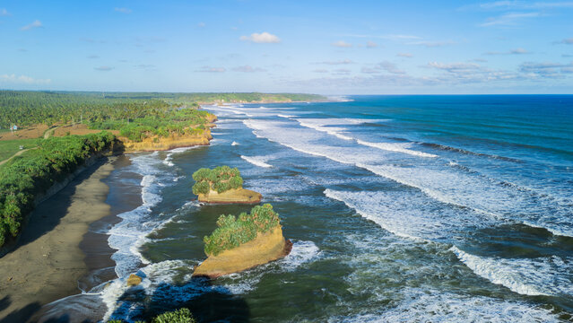 Aerial view of Ujung Genteng Beach featuring rocky islets, crashing waves, and lush tropical vegetation along the coastline in Sukabumi, West Java, Indonesia.