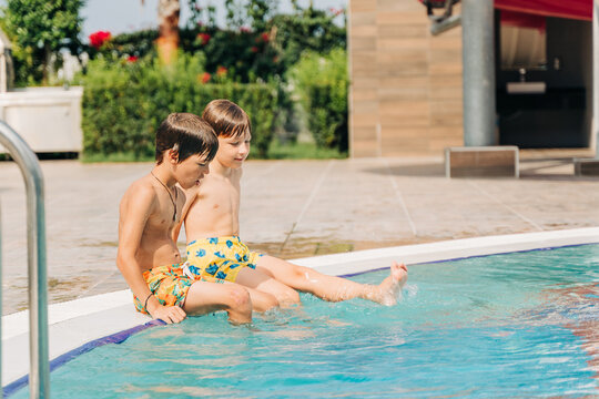 Two brothers Childs laughing while playing in swimming pool at sunny day. Kids friends boys refreshing at heat weather, active vacation and healthy lifestyle. Happy summer.