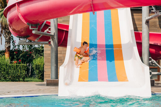 Child boy laughing while slide in pool after going down water slide at sunny day in water Aqua park. Kid refreshing at heat weather, active vacation and healthy lifestyle. Happy summer.