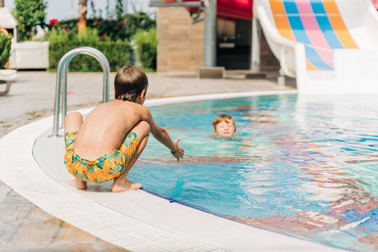 Two brothers Childs jumping and playing in swimming pool at sunny day. Kids friends boys refreshing at heat weather, active vacation and healthy lifestyle. Happy summer.