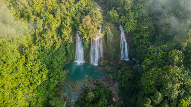 Aerial view of Cikaso Waterfall with its three distinct cascades falling into a turquoise pool surrounded by lush tropical forest and morning mist in Sukabumi, West Java, Indonesia.