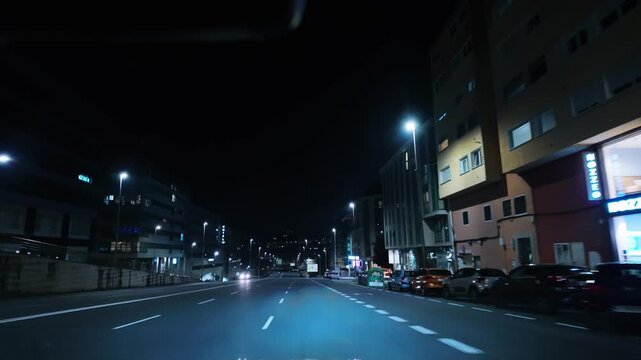 Point of view shot driving a car through the streets of a city at night. Empty roads and bright streetlights illuminate the asphalt, creating a cinematic and moody atmosphere in the darkness
