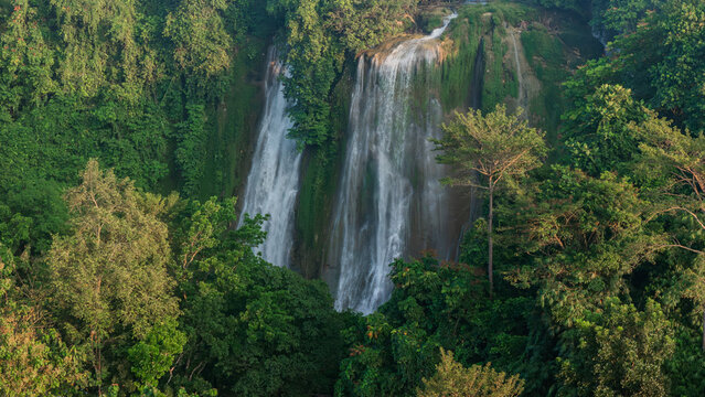 Aerial view of Cikaso Waterfall with multiple cascading streams falling down a rocky cliff surrounded by lush tropical jungle and dense green trees, Sukabumi, West Java, Indonesia.