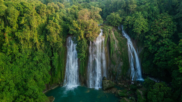 Aerial view of Cikaso Waterfall with three powerful cascades falling into a turquoise pool surrounded by dense tropical jungle in Sukabumi, West Java, Indonesia.