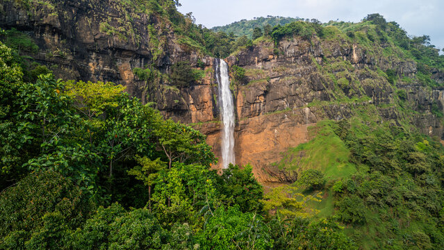 Aerial view of Cikanteh Waterfall cascading down a steep rocky cliff surrounded by lush tropical forest and dense green vegetation Sukabumi, West Java, Indonesia.