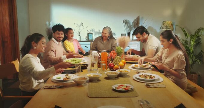 Indian happy relax joint family group sitting around table eat food talk speak share meal have fun joy Young adult male female aged mom girl boy child spend time enjoy night dinner room home place