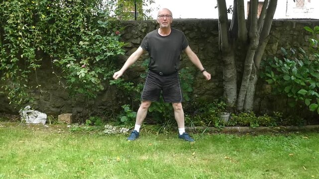 Elderly man doing high-intensity interval training jump squats in his backyard garden
