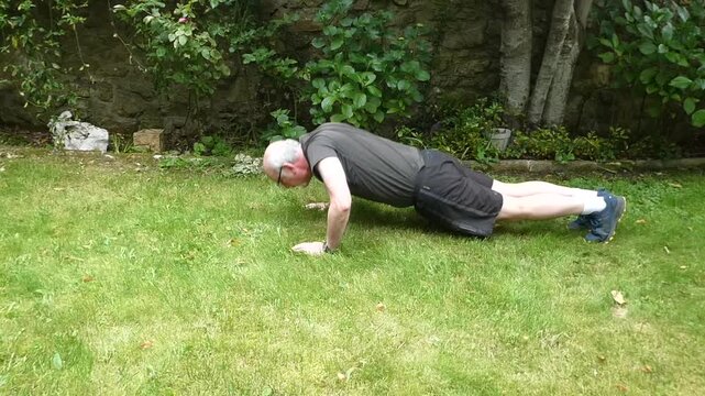 Elderly man doing strength training push-up exercises outdoors on the green grass