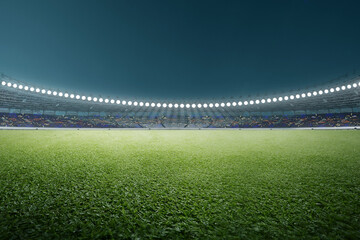 Wide angle view of a professional sports stadium at night, brightly lit by floodlights with a lush green grass field in the foreground and empty stands © Leo Lintang