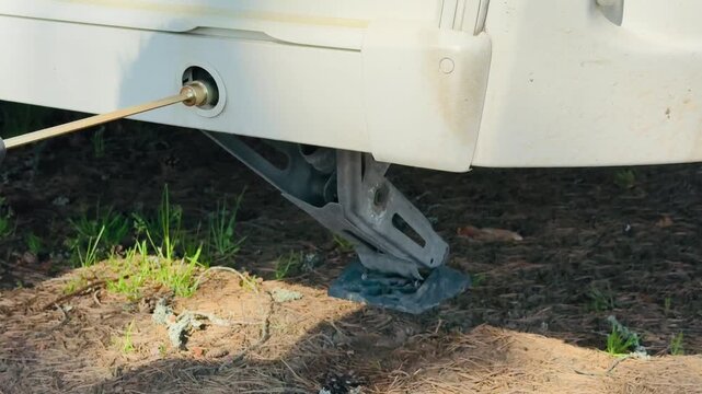 Cordless drill with adapter lifting a caravan stabilizer jack leg on a sunny camping site