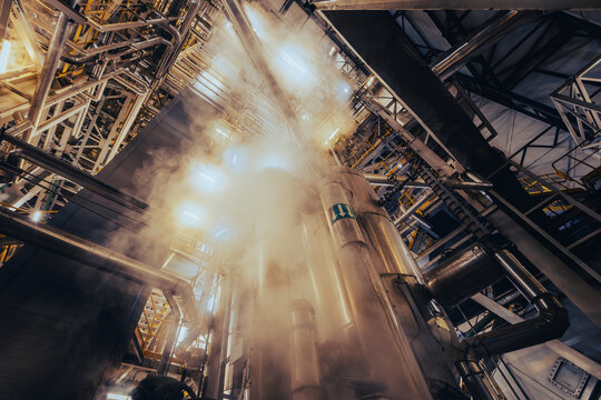 Upward view of industrial pipes with steam and steel structures