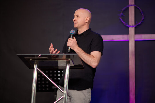 Emotional Christian preacher speaking with microphone and gesture church during worship gathering