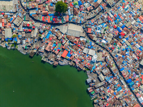 Aerial view of densely packed colorful corrugated metal rooftops of an informal settlement along the green waters of the coast in Monrovia, Liberia.