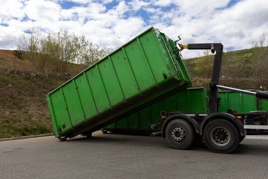 Hook lift truck unloading industrial waste container at recycling facility
