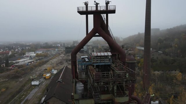 Drone passes under the blast furnace and curves downward past tanks and silos in heavy mist