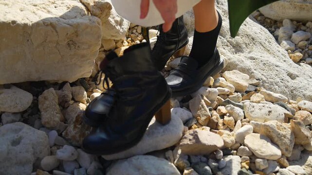Boots loafers rocks woman in a white dress picking up black leather boots on a rocky coastline outdoors during daylight