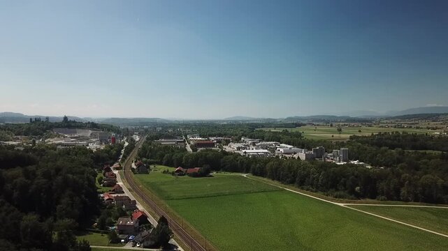Forward drone move follows the rail corridor toward the Lyss industrial zone from a slightly elevated angle