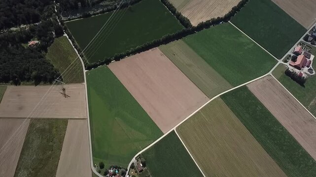 Top down drone flight crosses fields, pylons and river corridor before tilting up toward Lyss industrial area