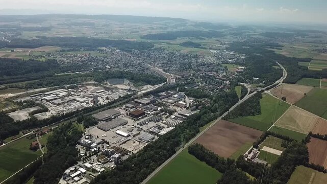 Wide elevated drone pullback reveals Lyss town, industrial district, highway and quarry in a broad landscape view