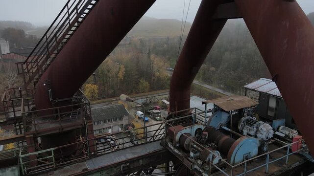Tight drone flyby reveals winch, pipes and upper furnace details from a close oblique industrial perspective