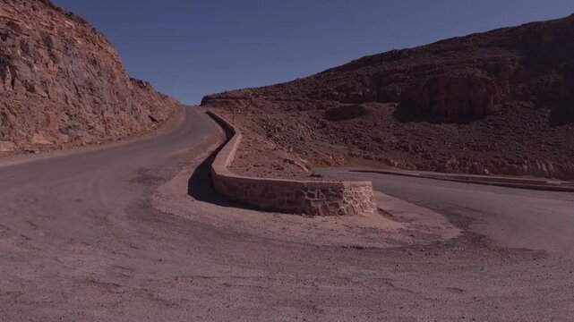 Empty winding road curving through a rocky arid Atlas Mountain pass with a stone road divider