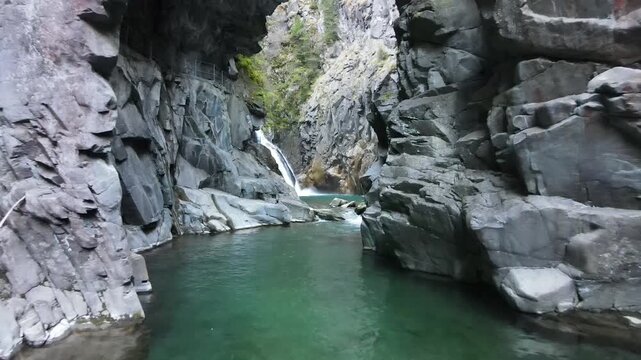 Careful forward drone move through stone caverns along the creek approaching the waterfall deep inside the gorge.