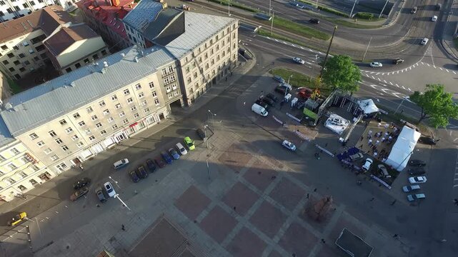 Aerial high angle view of an urban plaza in Riga Latvia during a sunny summer morning featuring historic buildings with grey and orange roofs beside an outdoor event setup with white tents