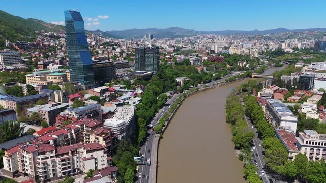 aerial panorama of the Kura River (Mtkvari) flowing through central Tbilisi, Georgia, lush riverbank parks, and the modern Biltmore Hotel skyscraper on the on the skyline