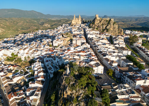 Aerial view of the white-washed houses of Olvera with the historic church and castle perched on a rocky hill under a clear blue sky Olvera, Andalusia, Spain.