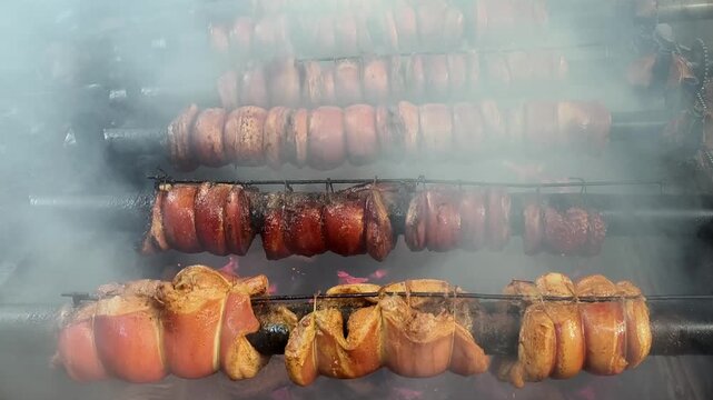 Traditional Balinese samsam guling pork belly roasting on a rotisserie spit over smoky charcoal