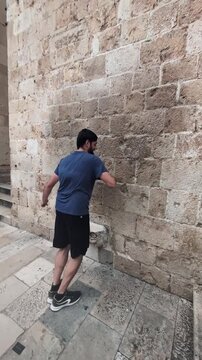 Young tourist attempting the legendary Mascaron balancing challenge on the Franciscan Monastery wall in the Old Town of Dubrovnik, Croatia, an ancient local superstition