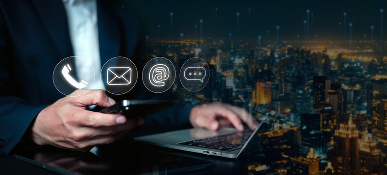 Businessman using smartphone and laptop with contact icons for customer support, email communication and digital networking in smart city technology and online business concept.