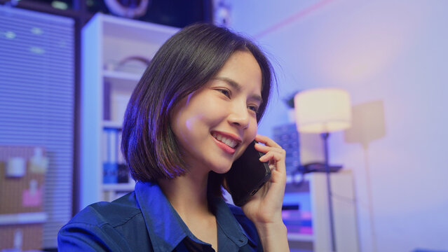 Smiling young Asian businesswoman talking on smartphone in office.