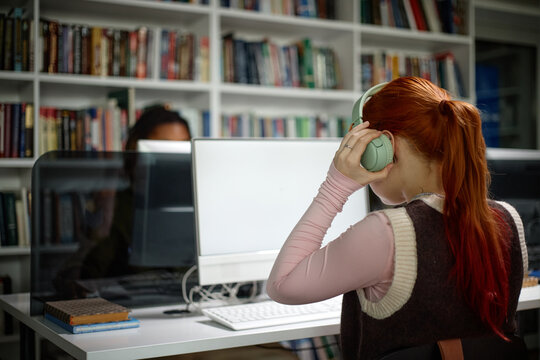 Student wearing headphones, studying at desktop computer in library, focusing on digital learning and research
