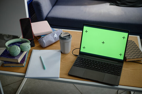 Student workspace showing laptop with green screen, notebook, books, headphones, smartphone, coffee cup, supporting online learning, study planning, education marketing
