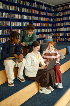 Vertical shot of diverse students collaborating on laptop in library, studying and sharing ideas. Education teamwork concept for school marketing, e learning, youth programs
